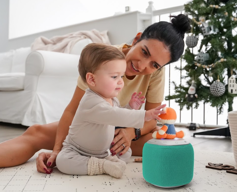 Mother and baby playing together next to a Christmas tree.